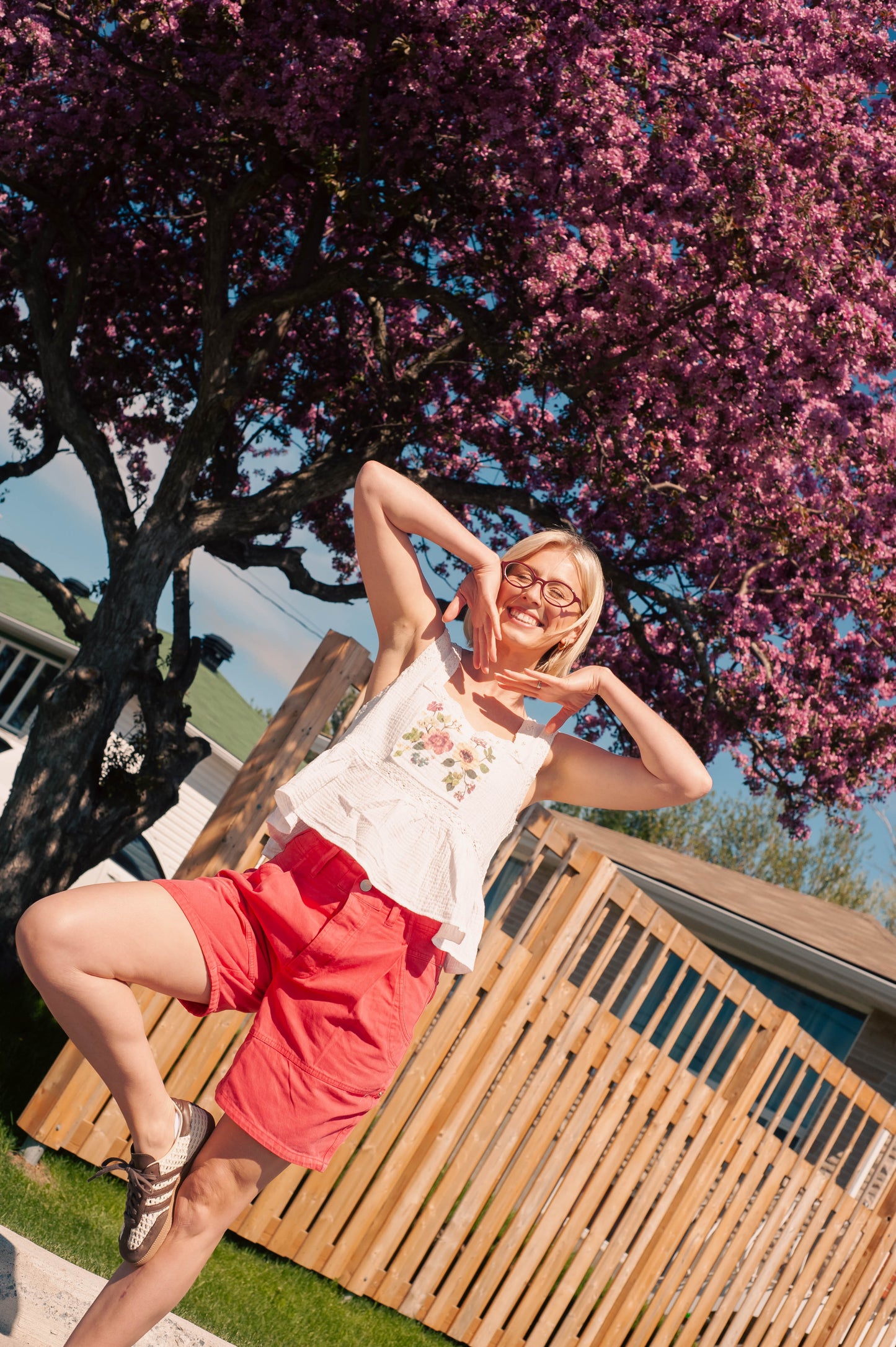 women wearing red shorts and a white floral top against a fence and floral tree