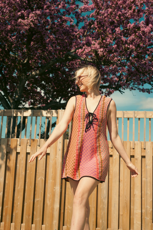 Woman in a colorful dress standing outdoors with a wooden fence and flowering tree in the background