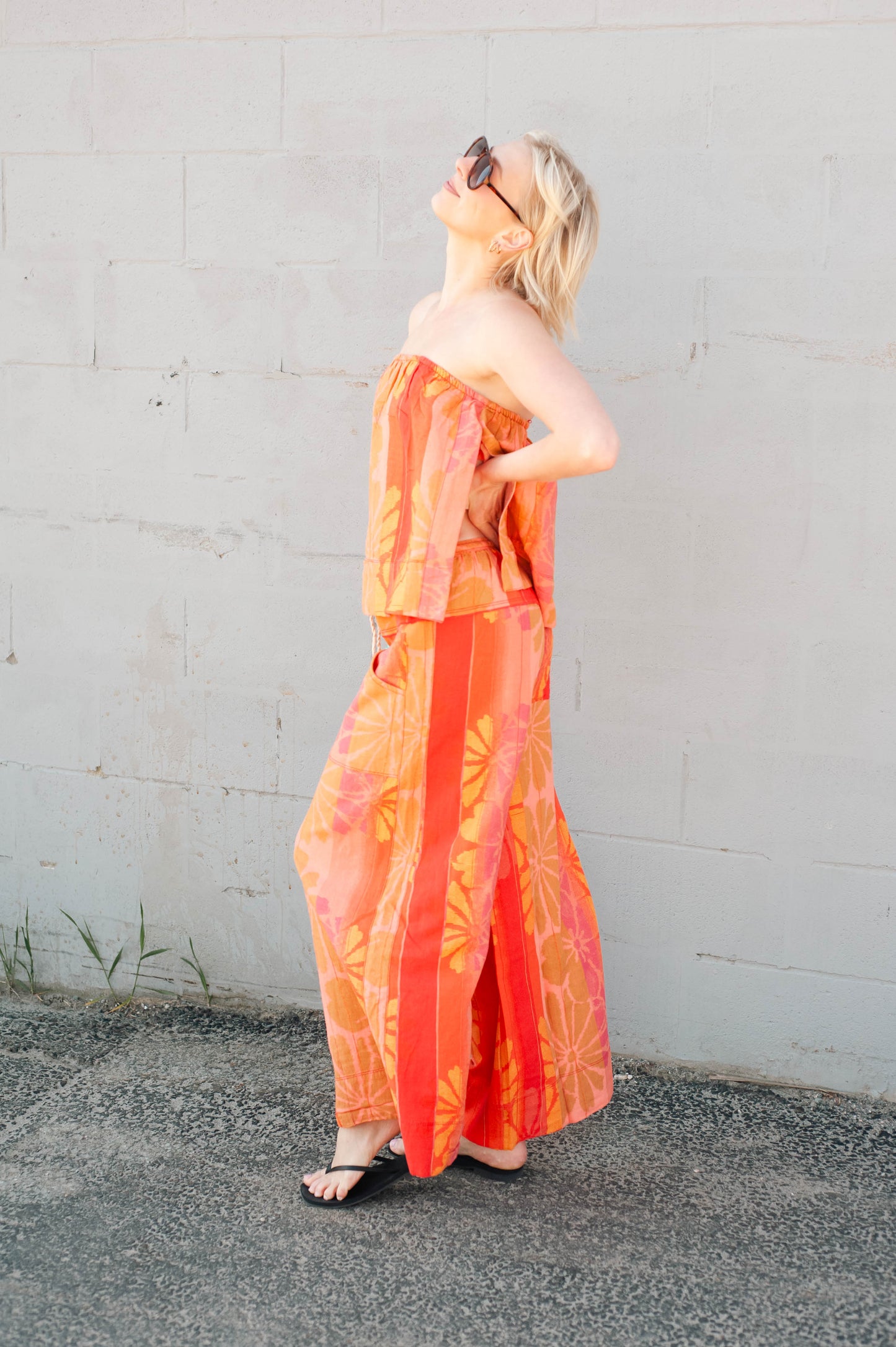 Woman wearing an orange strapless dress against a gray wall.