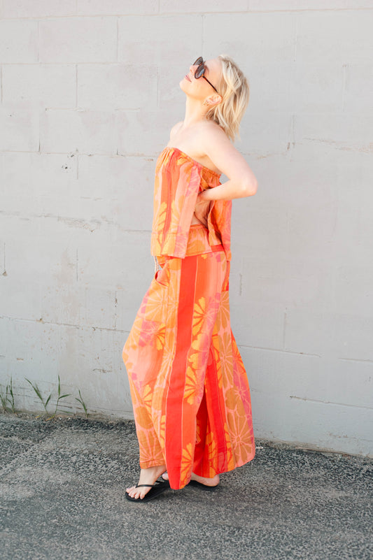 Woman wearing an orange strapless dress against a gray wall.