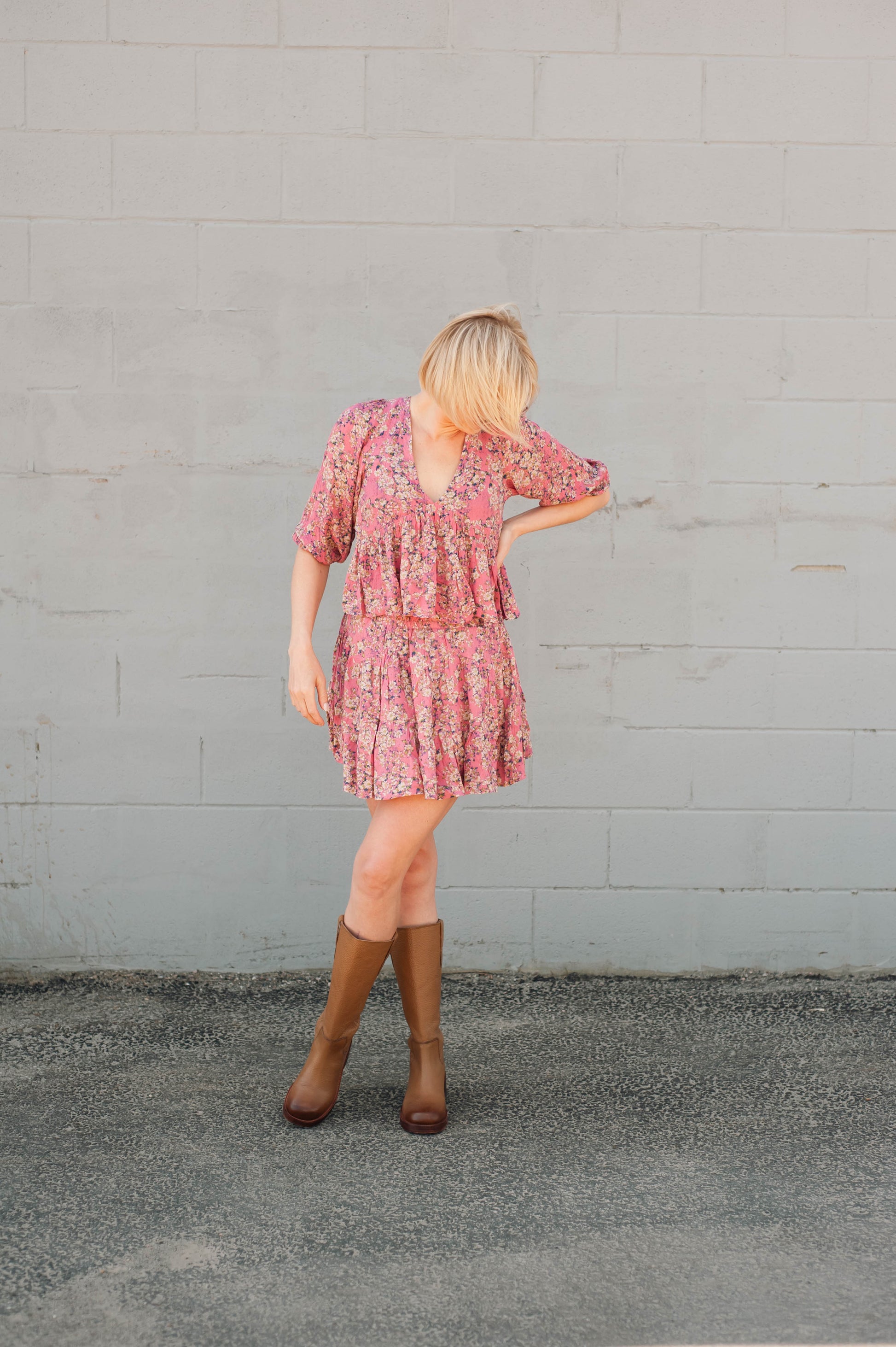 Woman wearing a pink floral dress and brown boots against a gray wall.