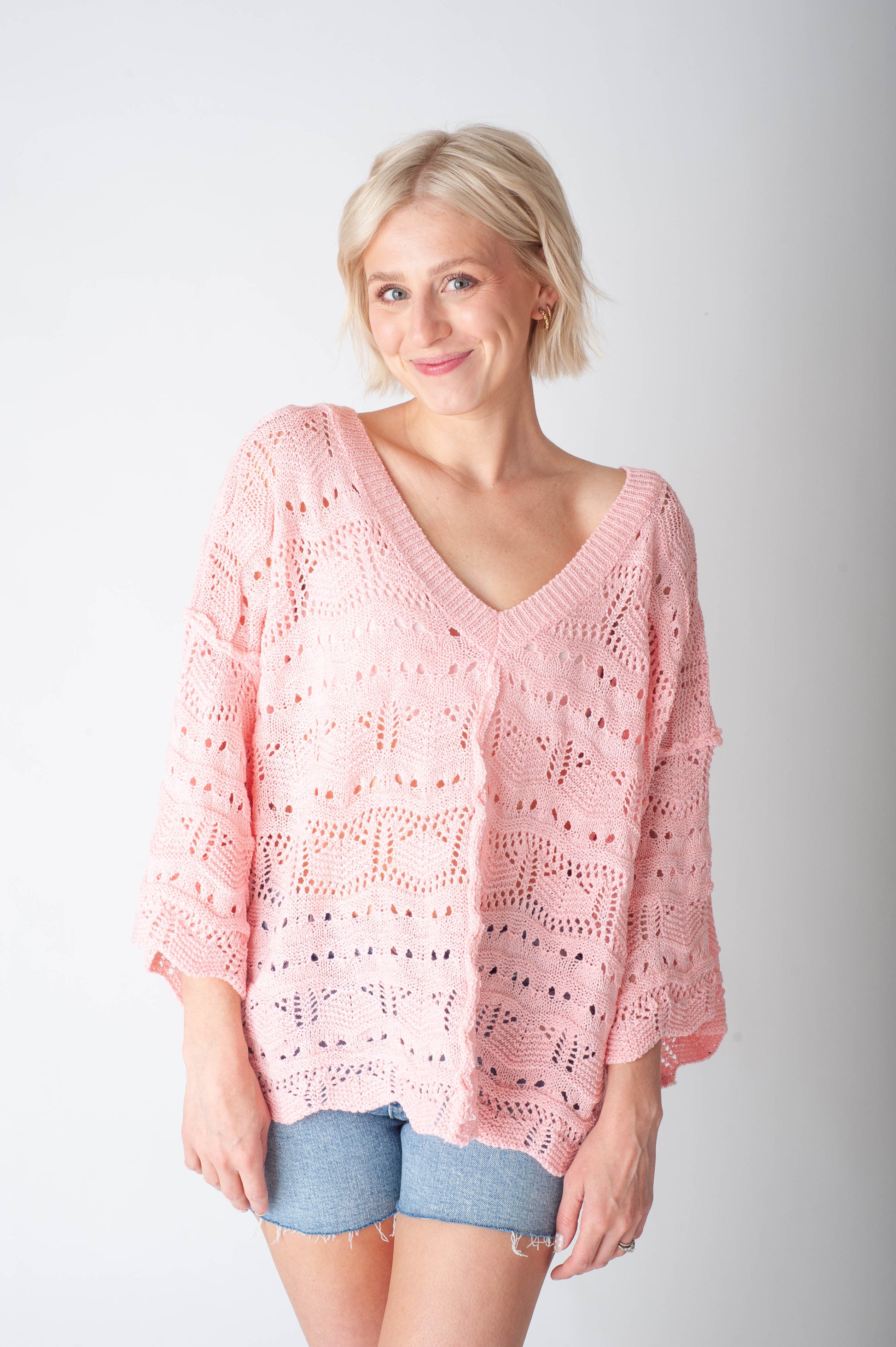 Women wearing a pink crochet sweater and denim shorts on a neutral background.