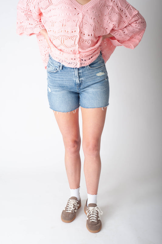 Women wearing long denim shorts and a pink sweater. 