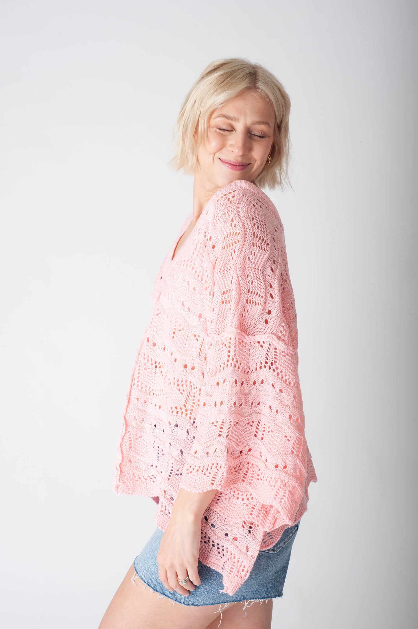 Women wearing a pink crochet sweater and denim shorts on a neutral background.