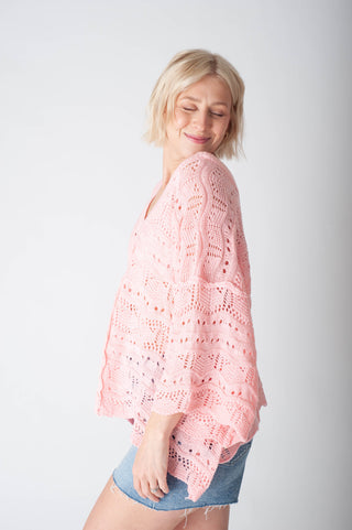 Women wearing a pink crochet sweater and denim shorts on a neutral background.