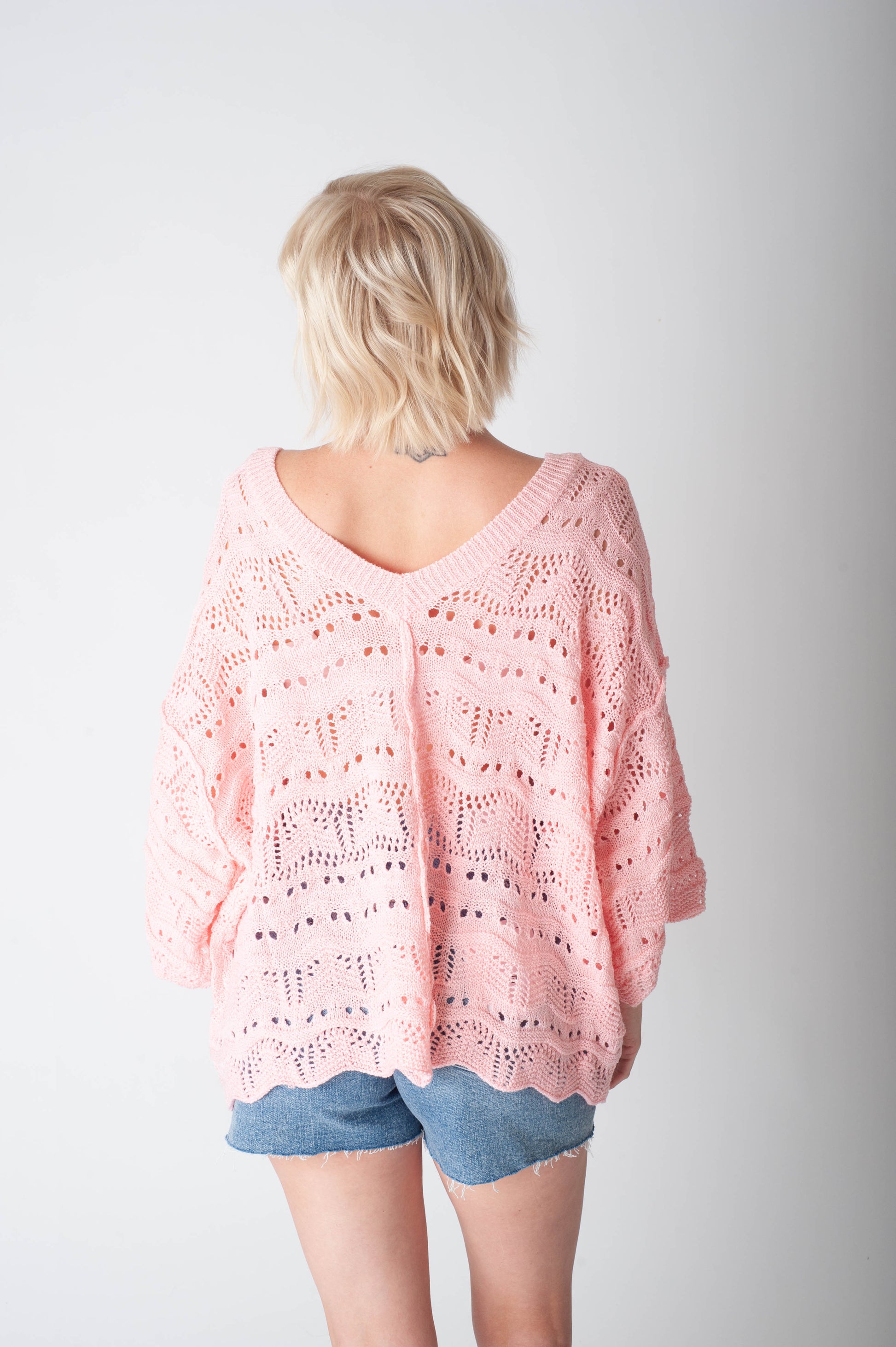 Women wearing a pink crochet sweater and denim shorts on a neutral background.