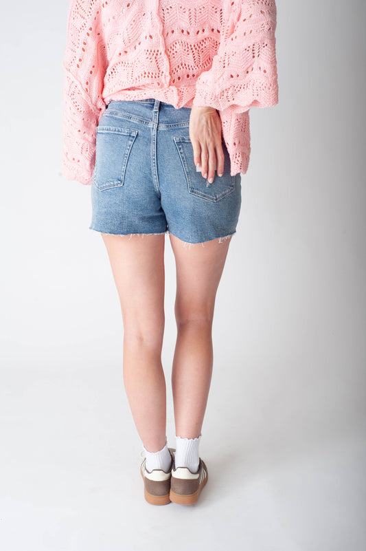 Women wearing long denim shorts and a pink sweater. 