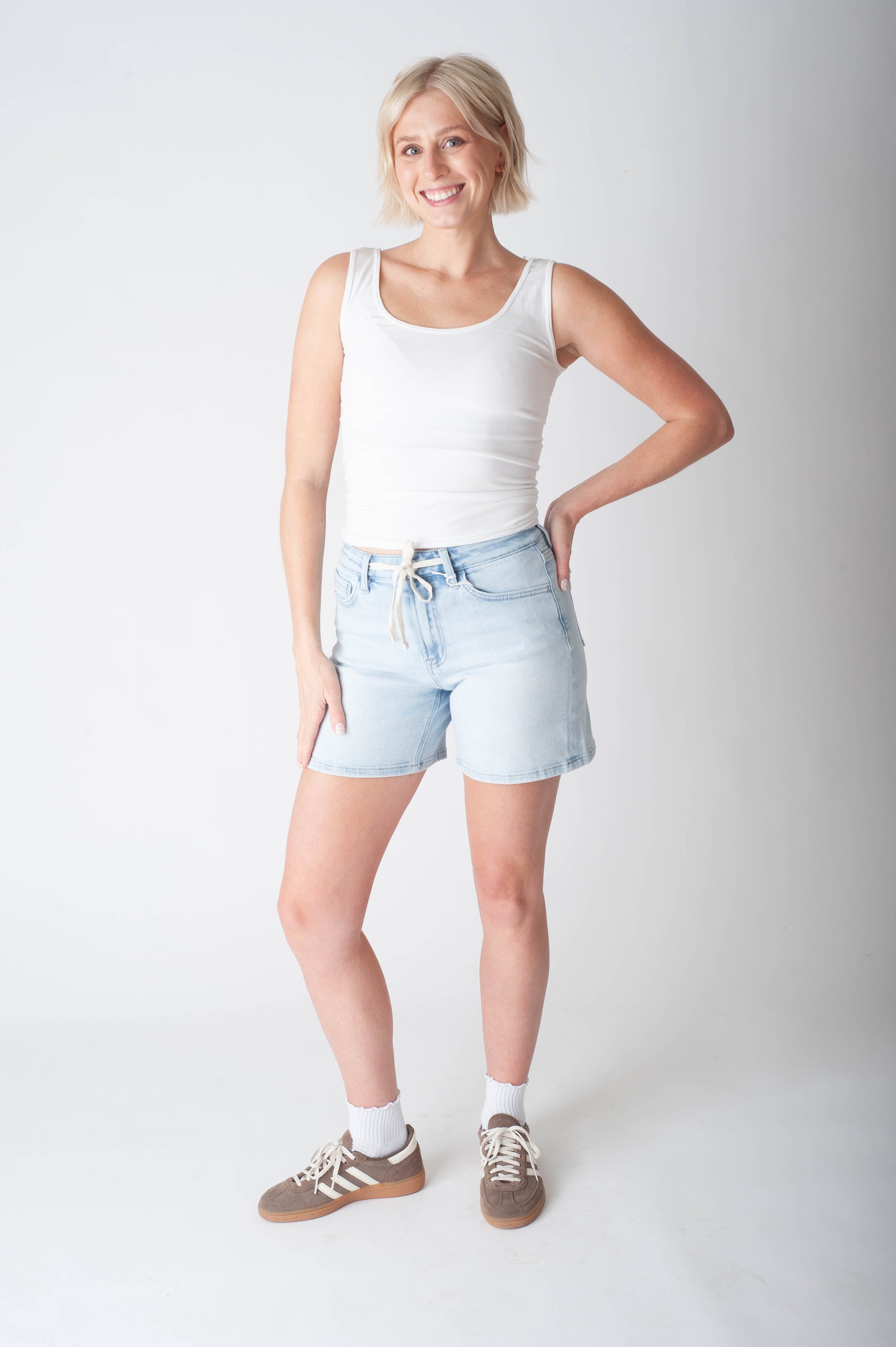 Women wearing long denim shorts and a white tank top.