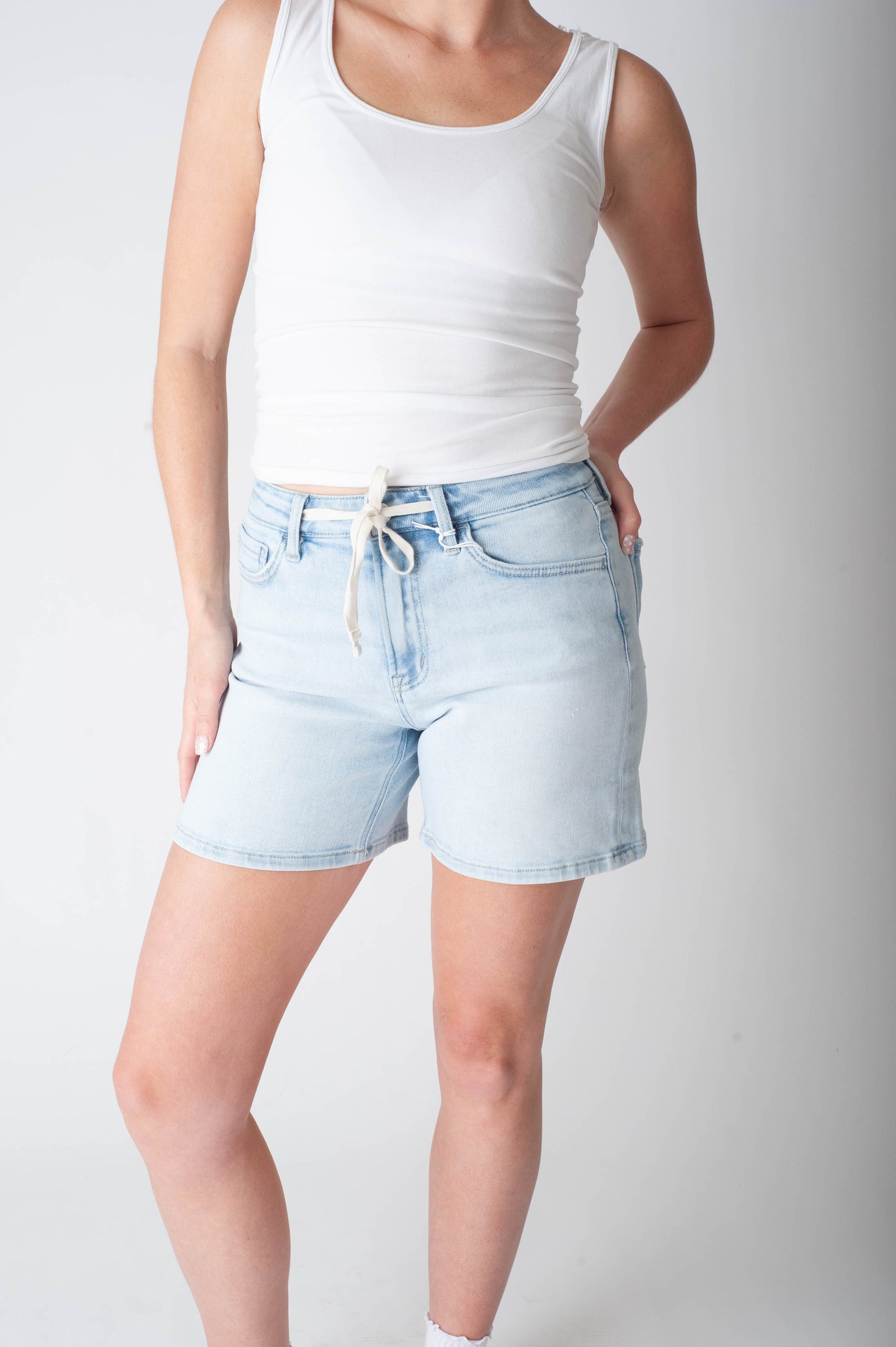 Women wearing long denim shorts and a white tank top.