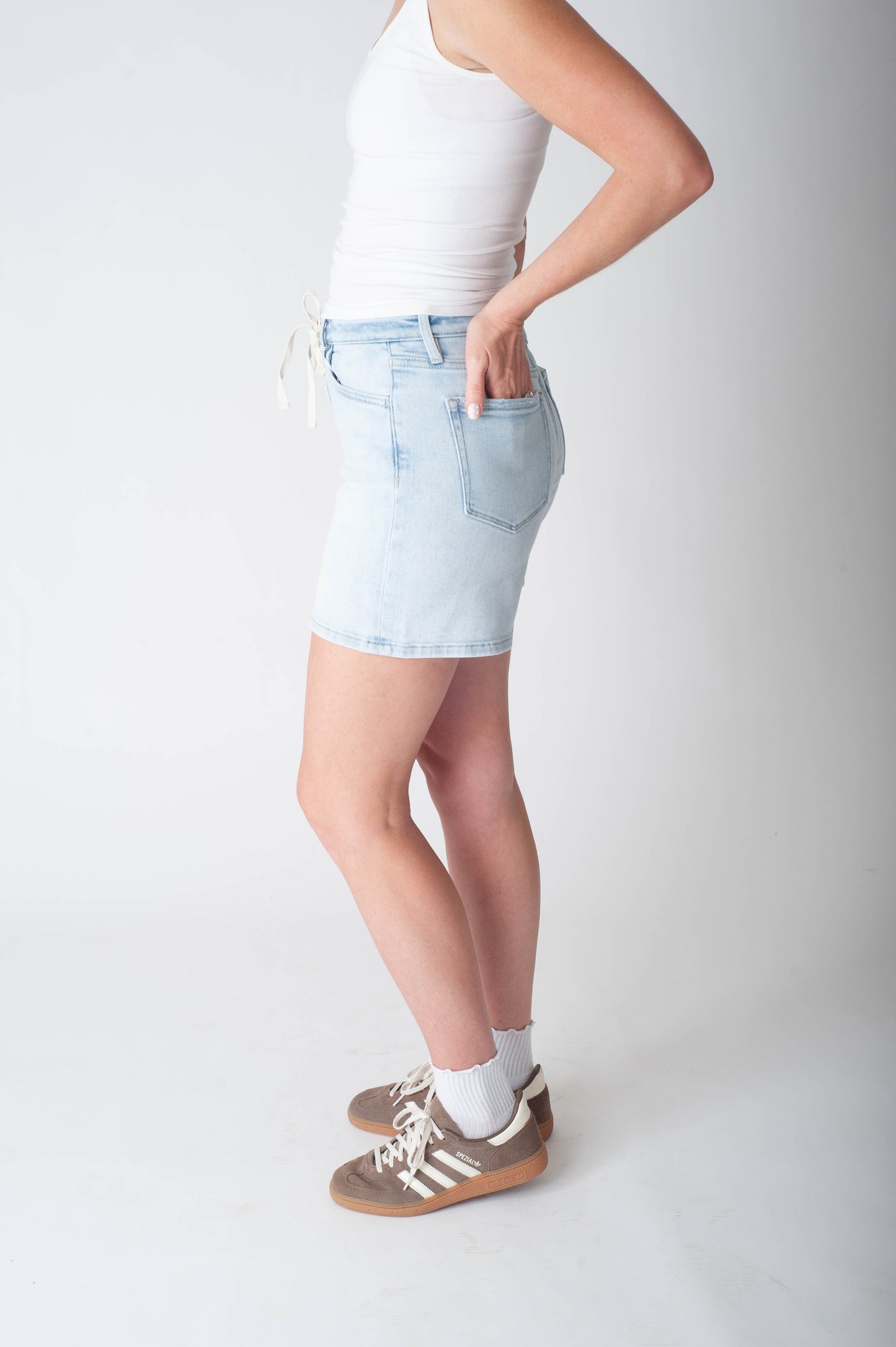 Women wearing long denim shorts and a white tank top.