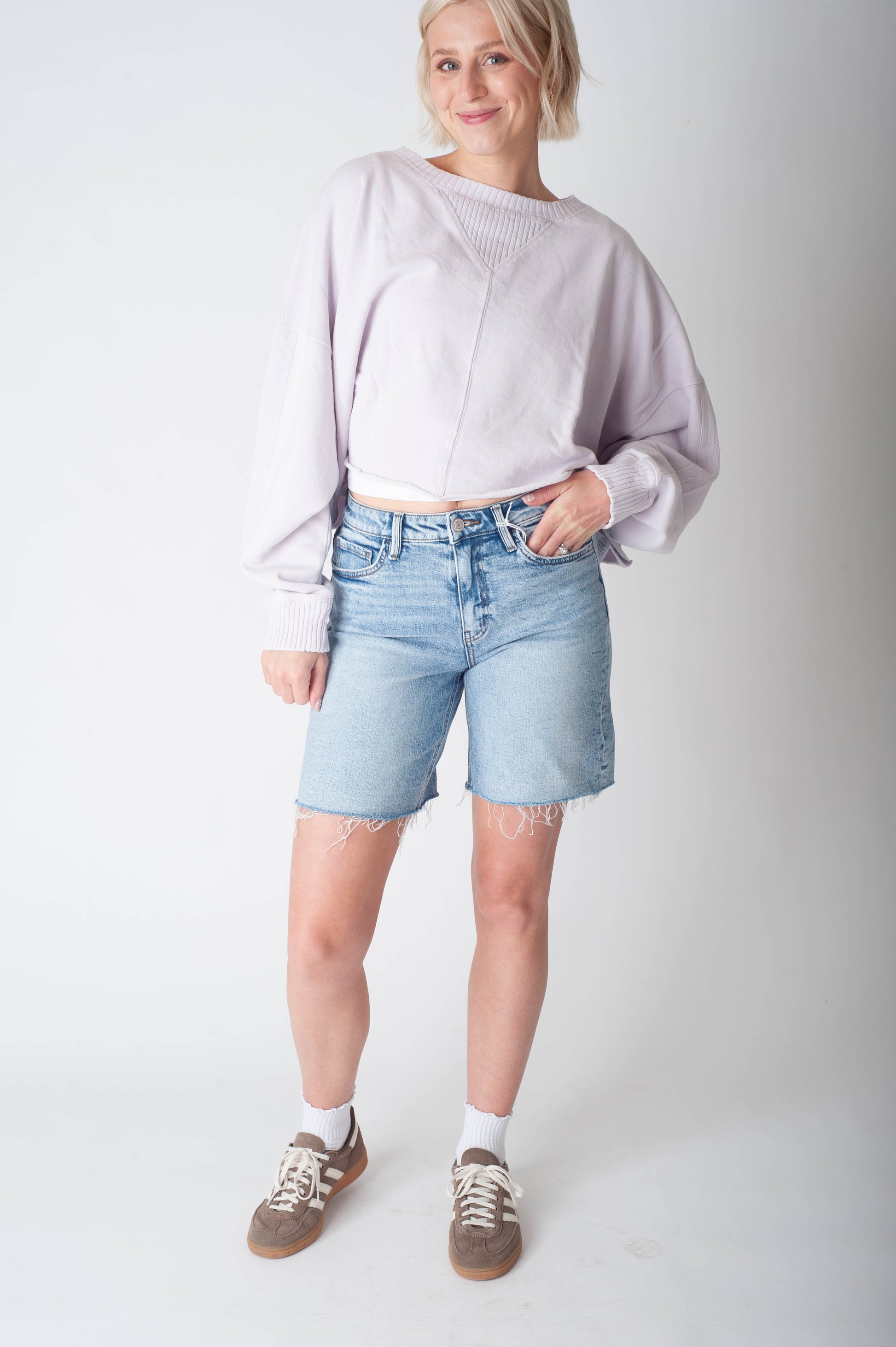 Women wearing long denim shorts and a purple sweater. 