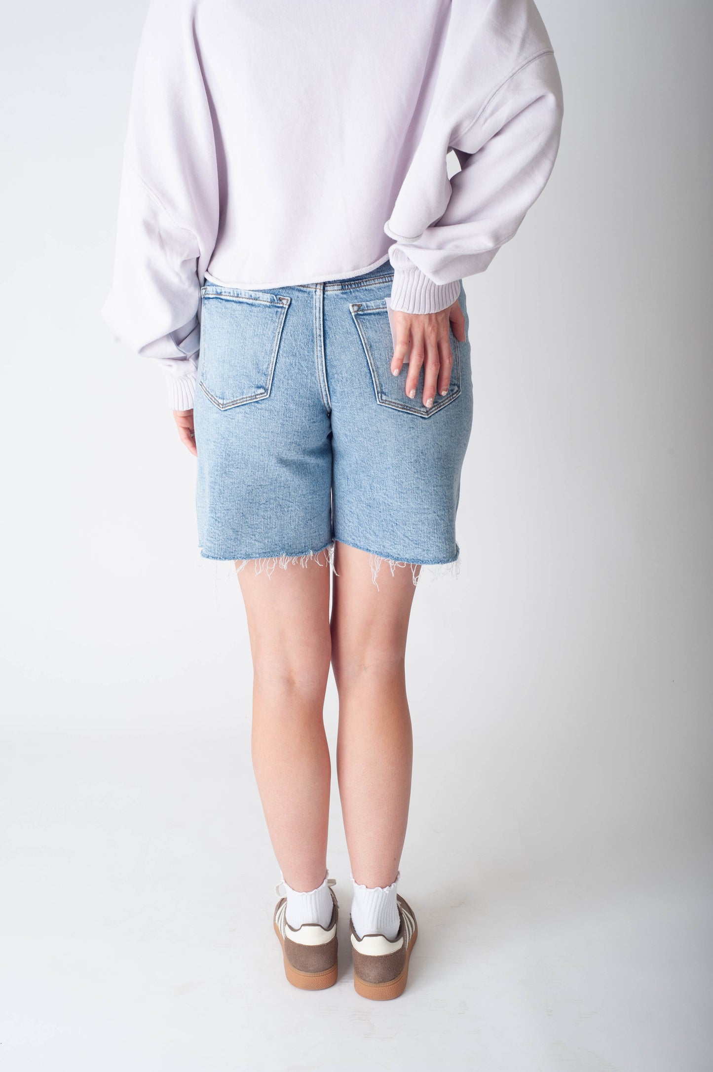 Women wearing long denim shorts and a purple sweater. 