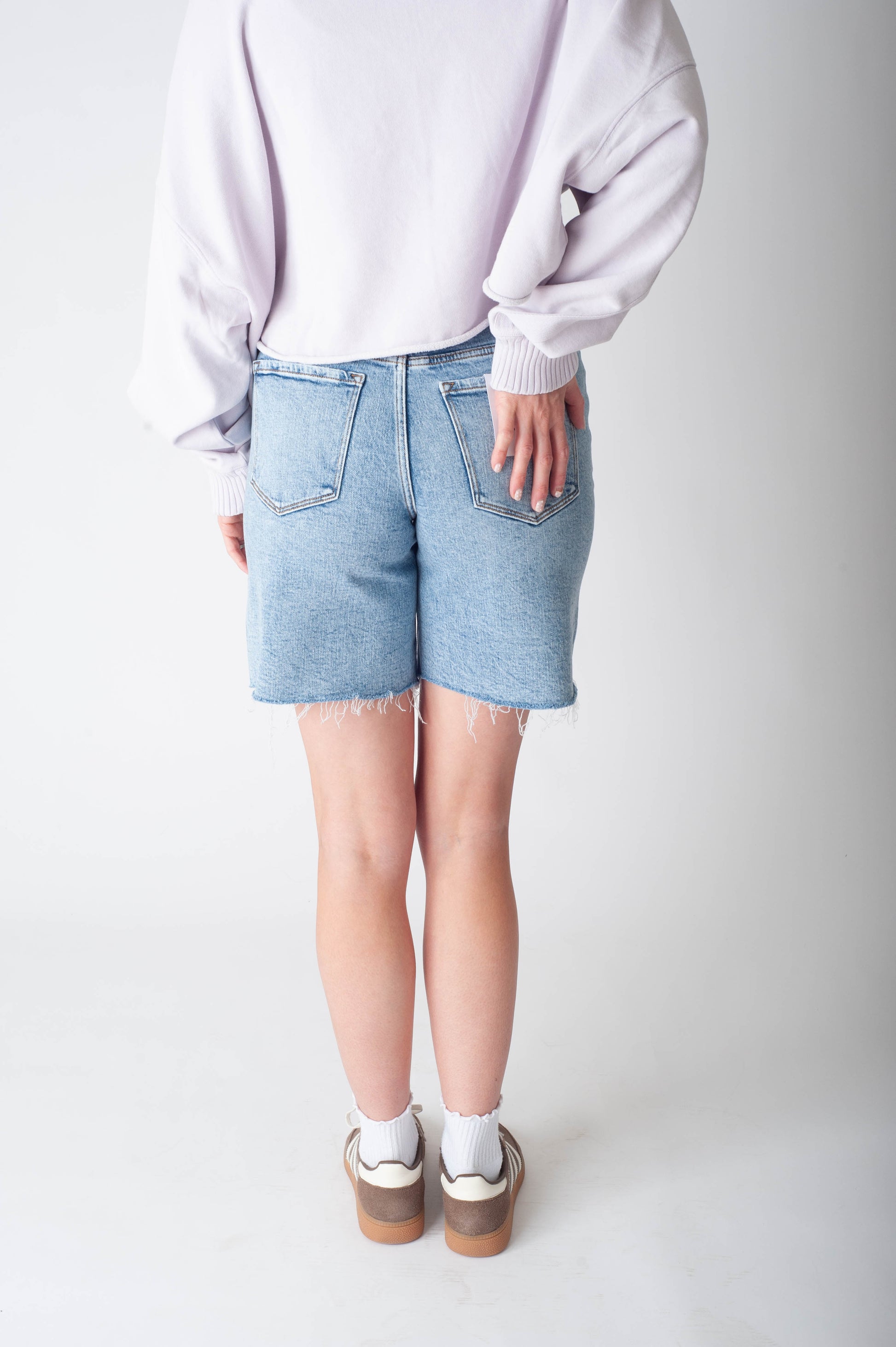 Women wearing long denim shorts and a purple sweater. 