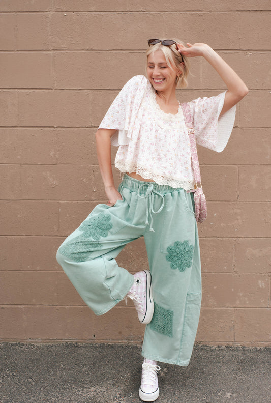 Women wearing a wide leg barrel pant with floral crochet patches allover and a floral top.