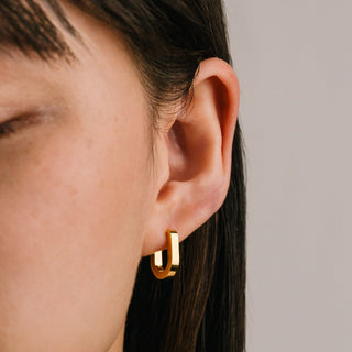 Close-up of an ear wearing a gold hoop earring with a neutral background