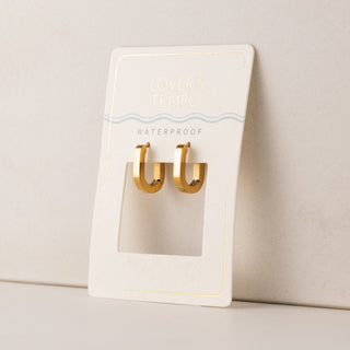 Gold earrings on a white card with 'Waterproof' text on a beige background