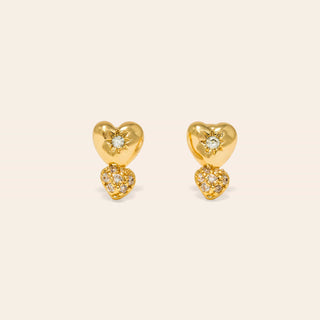 Gold heart-shaped earrings with embedded stones on a beige background