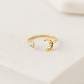 Gold open ring with moon design on a light beige background