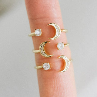 Gold crescent moon and diamond rings on a finger against a neutral background