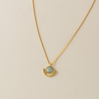 Gold necklace with a green pendant on a beige background