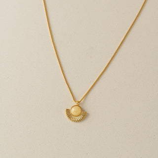 Gold necklace with a sun-shaped pendant on a beige background