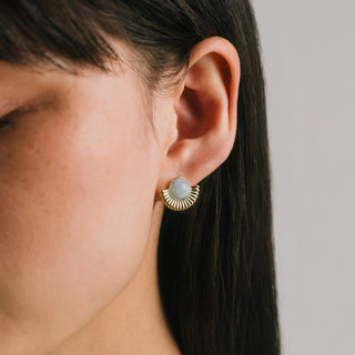 Close-up of an ear wearing a gold earring with a gray gemstone on a neutral background