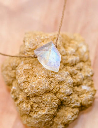 Necklace with a large, faceted gemstone held over a rough-textured stone.