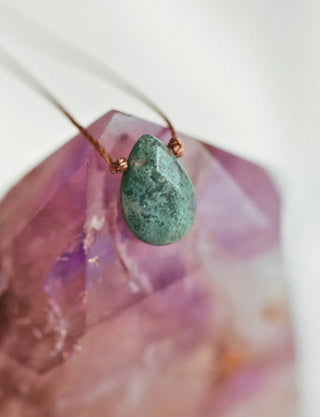 Green teardrop pendant on a chain against a blurred background