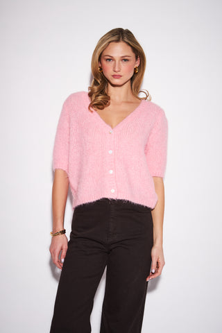 A women wearing a fuzzy pink cardigan against a neutral background.