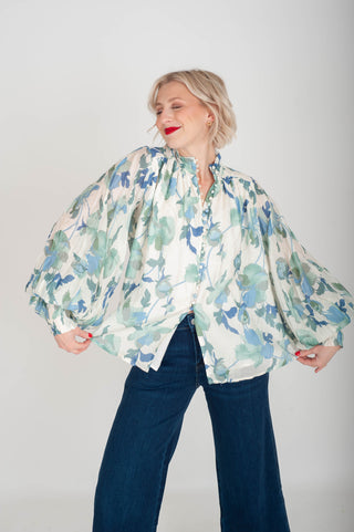 Woman wearing a floral blouse with wide sleeves against a plain background