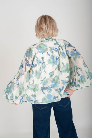 Person wearing a floral blouse with wide sleeves on a plain background