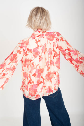 Person wearing a floral blouse with long sleeves and blue jeans on a white background