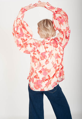 Person wearing a floral blouse with arms raised on a white background