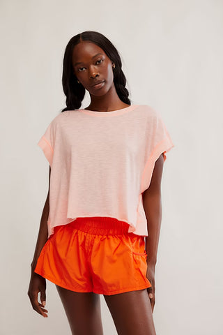 Woman wearing a light pink top and orange shorts on a plain background