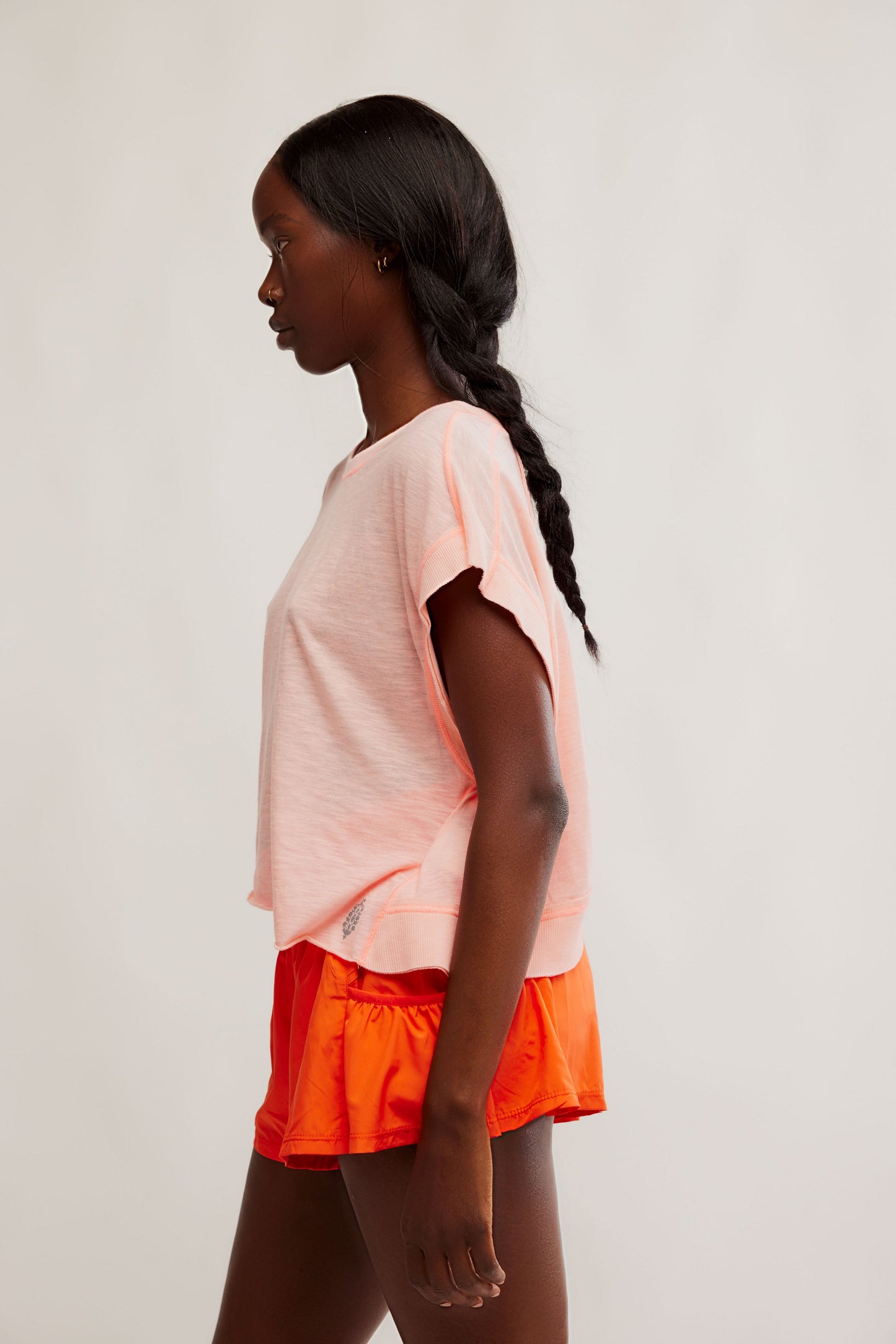 Woman wearing a peach top and orange shorts on a plain background