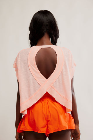 Person wearing a peach mesh top with cut-out design and orange shorts on a plain background