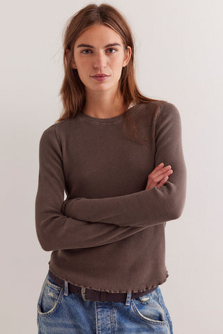 Woman wearing a brown sweater and blue jeans against a plain background