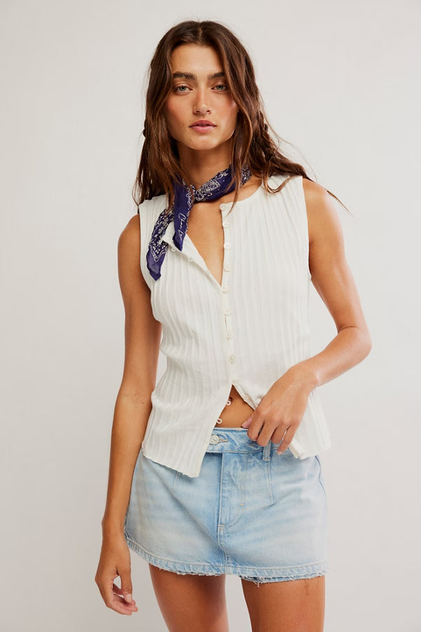 Woman wearing a white sleeveless top and denim skirt with a blue scarf on a plain background