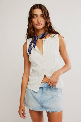 Woman wearing a white sleeveless top and denim skirt with a blue scarf on a plain background