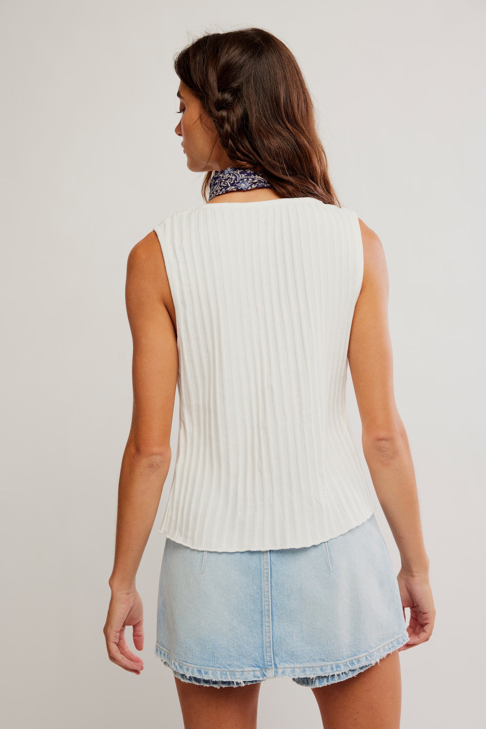 Woman wearing a white sleeveless ribbed sweater and light blue denim skirt on a plain background
