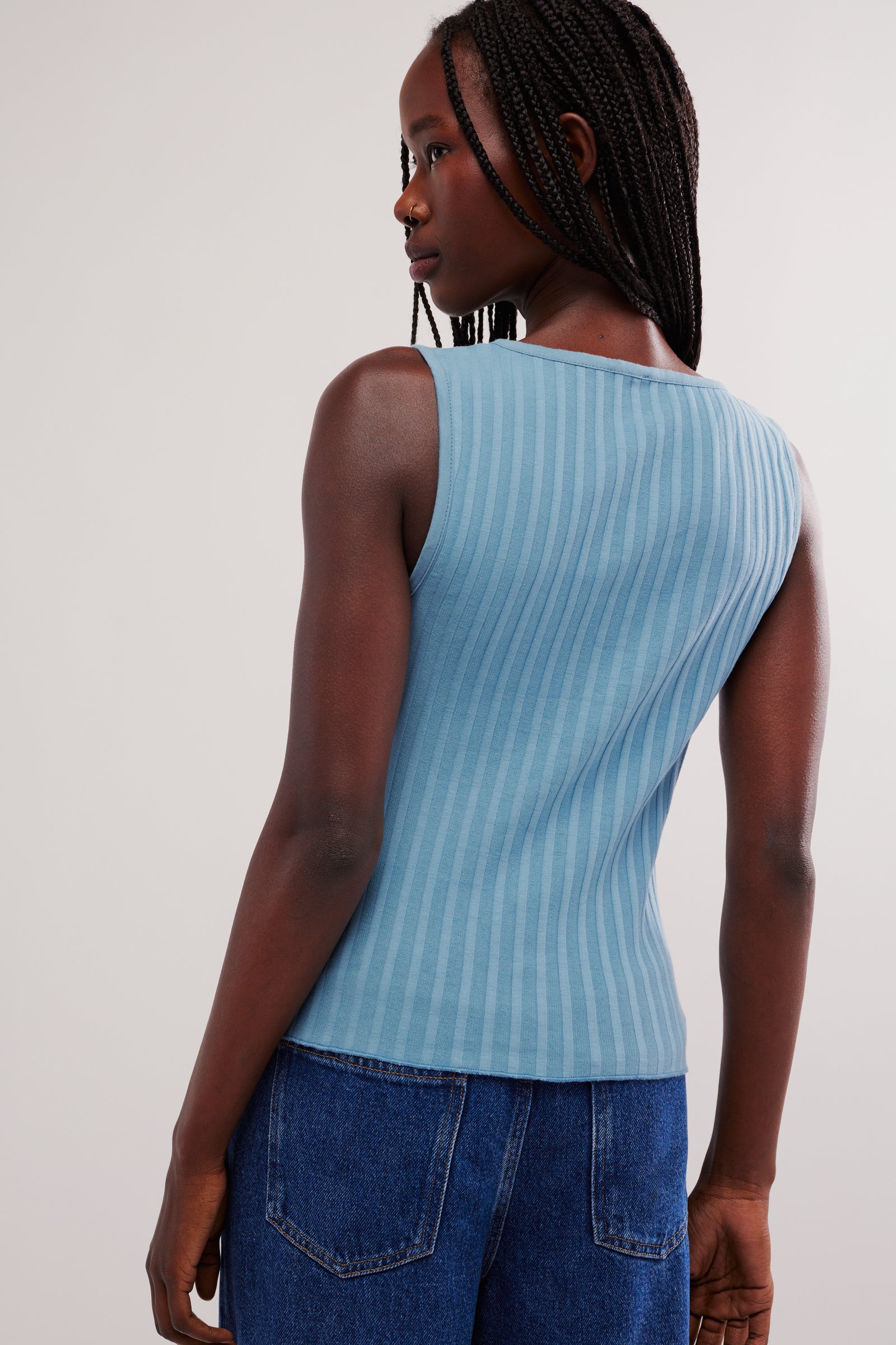 Person wearing a blue ribbed tank top and blue jeans on a white background