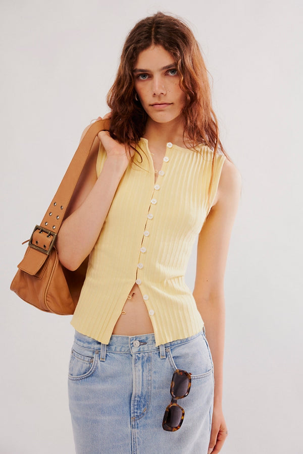 Woman wearing a yellow sleeveless top and blue jeans, holding a brown leather bag.