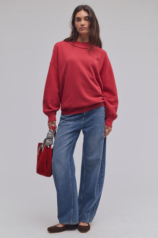 Person wearing a red sweater and blue jeans holding a red bag on a plain background