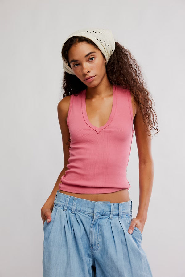 Woman wearing a pink tank top and blue jeans with a white headscarf against a plain background