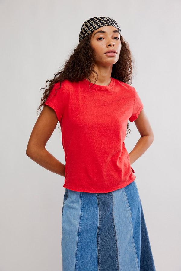 Woman wearing a red t-shirt and blue jeans with a patterned headband against a plain background