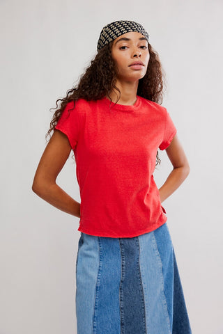 Woman wearing a red t-shirt and blue jeans with a patterned headband against a plain background