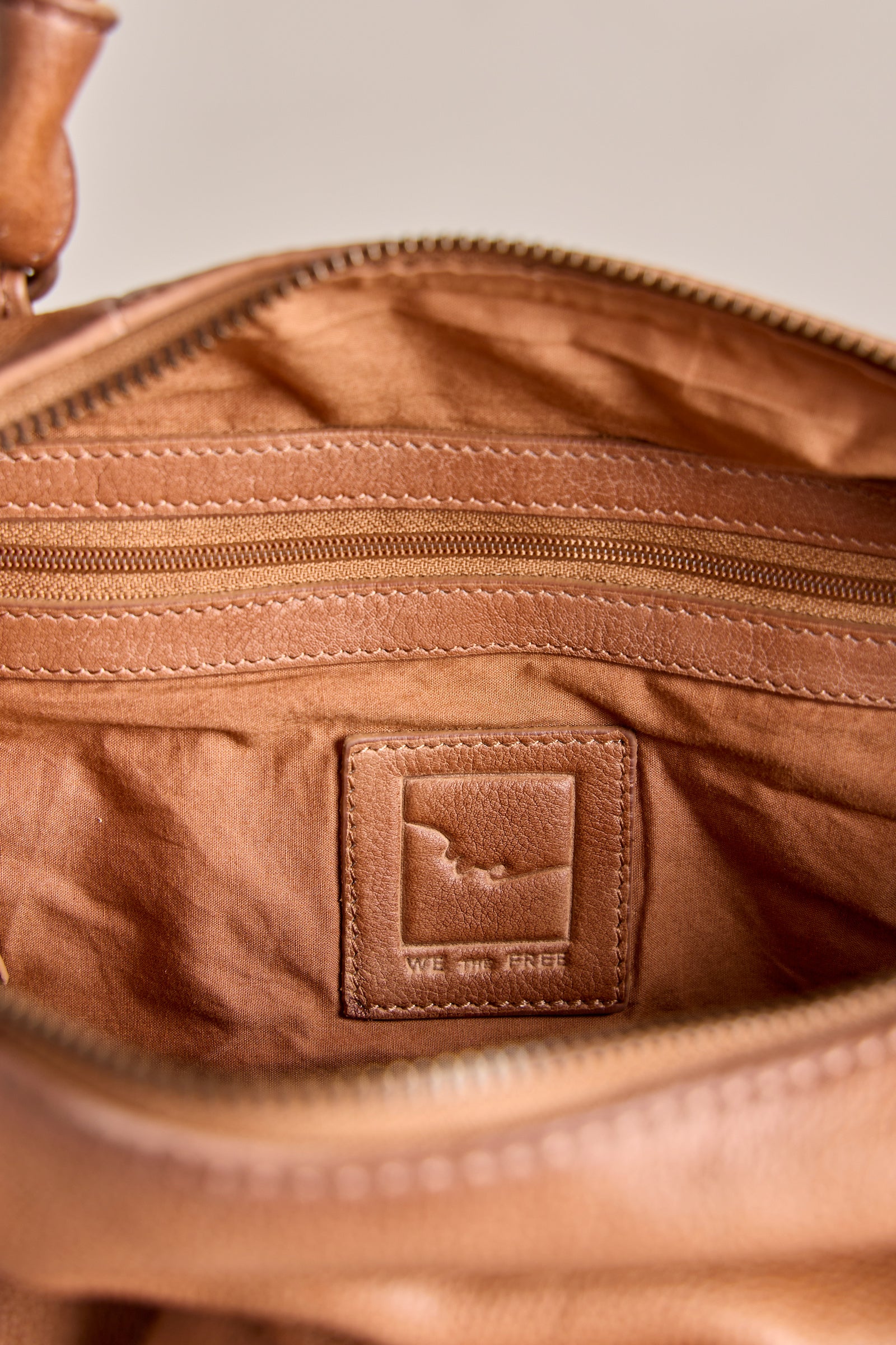 Close-up of a brown leather bag with a visible brand logo on a neutral background
