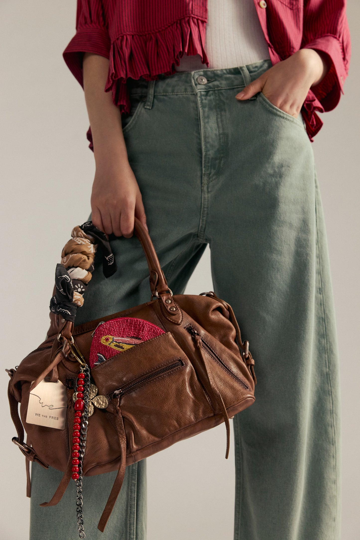 Person holding a brown leather bag with patches, wearing a red shirt and green pants.