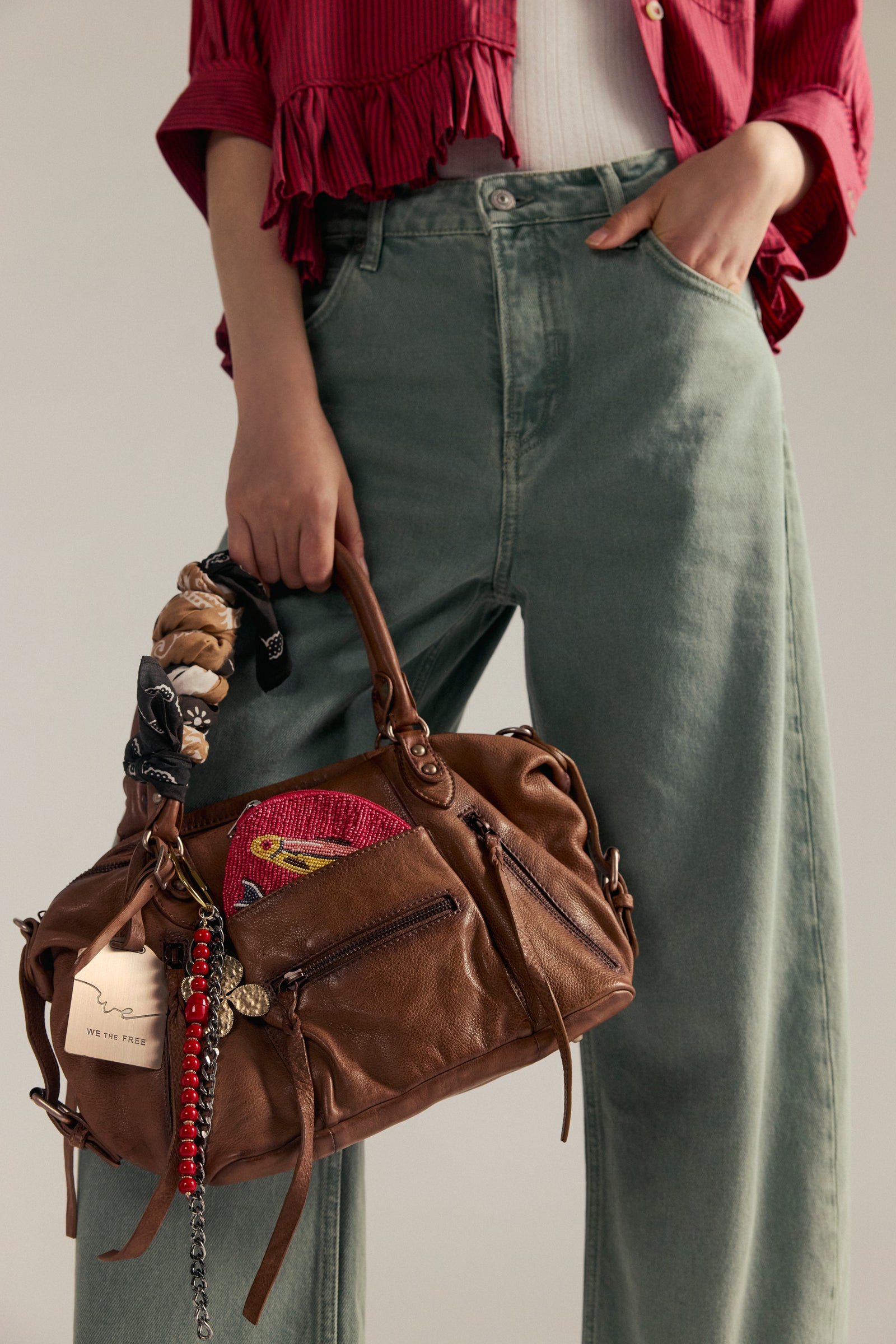 Person holding a brown leather bag with patches, wearing a red shirt and green pants.