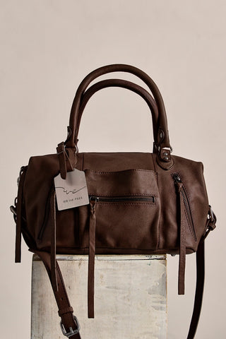 Brown leather handbag with a tag on a neutral background
